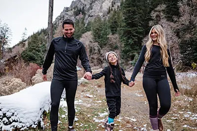 Family of three wearing winter gear walking together in a snowy mountain landscape